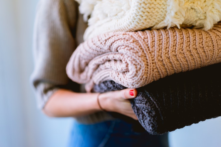 Idee fotografiche autunnali per Instagram - una ragazza con maglioni piegati in mano